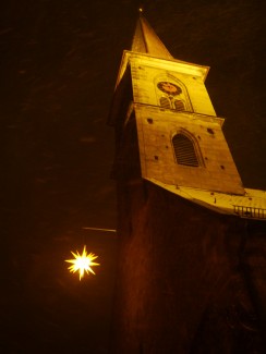 StBartholomäuskirche im wilden Schneetreiben des Nachts mit beleuchtetem Kirchturm und Herrnhuterstern, der vorm Turm hängt